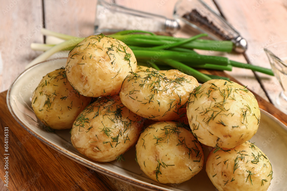 Plate of boiled baby potatoes with dill and green onion on white wooden background