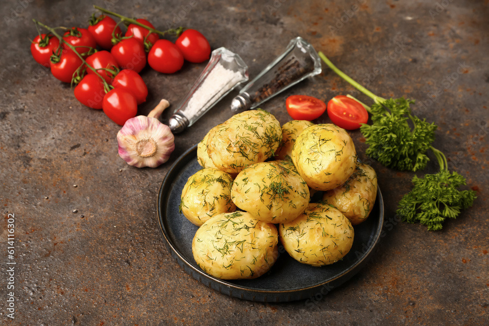 Plate of boiled baby potatoes with dill and tomatoes on dark background