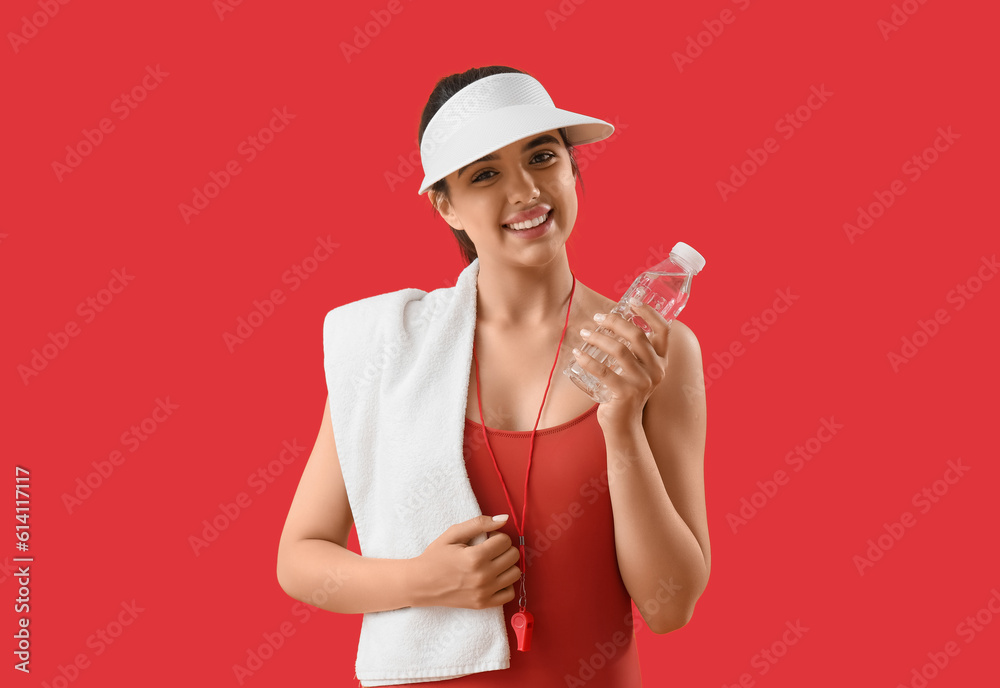 Female lifeguard with bottle of water on red background