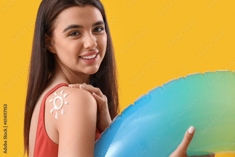 Young woman with sun made of sunscreen cream on her shoulder and inflatable ring against yellow back