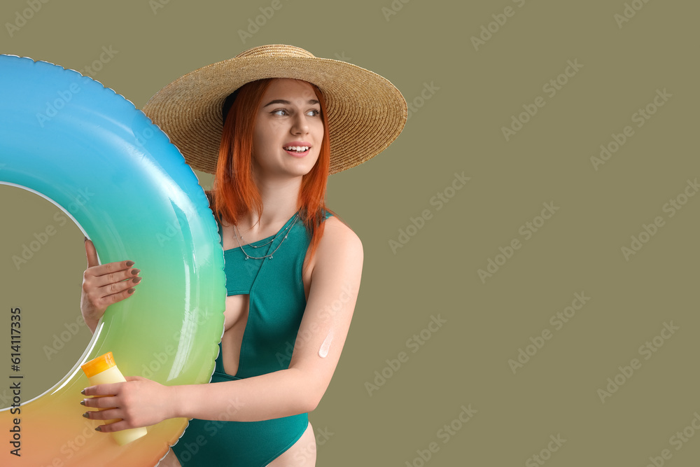 Young woman with sunscreen cream and inflatable ring on green background