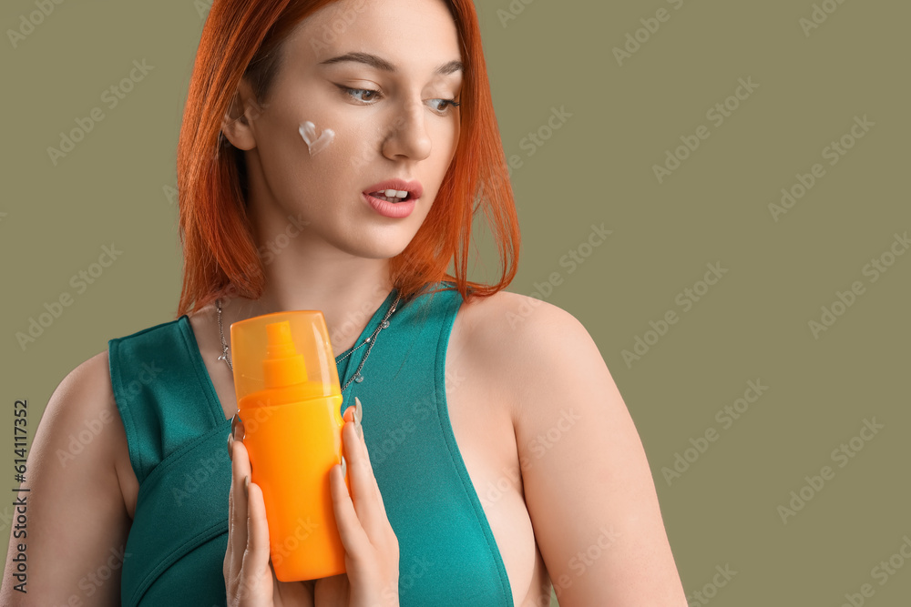 Young woman with heart made of sunscreen cream on green background