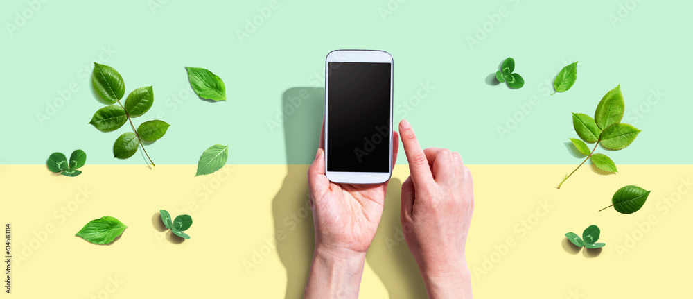 Person using a smartphone with green leaves - flat lay