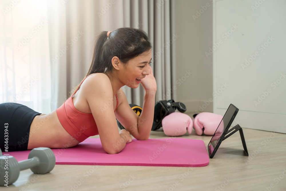 Sporty woman in sportswear doing exercise on fitness mat and using digital tablet having online trai