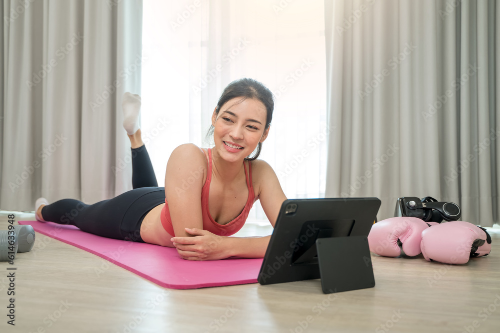 Sporty woman in sportswear doing exercise on fitness mat and using digital tablet having online trai