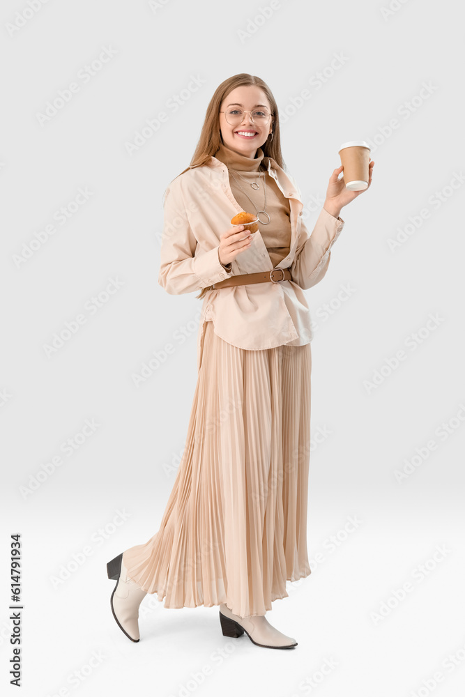 Young woman with tasty cupcake and cup of coffee on light background