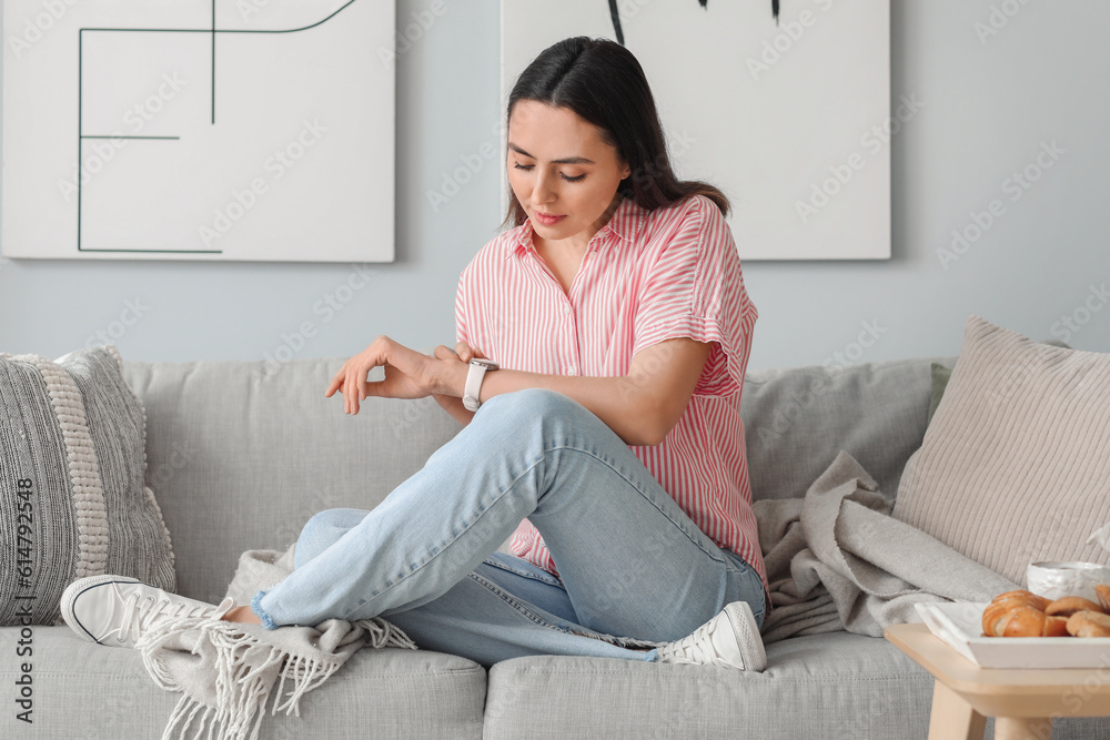 Young woman with stylish wristwatch sitting on sofa at home