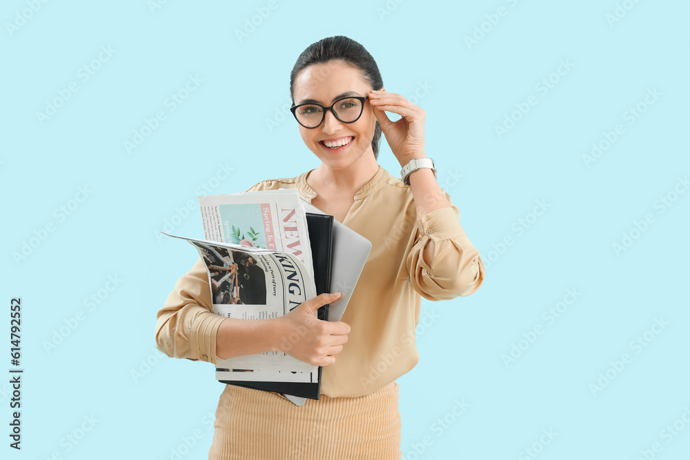 Young businesswoman with wristwatch, newspapers and laptop on blue background