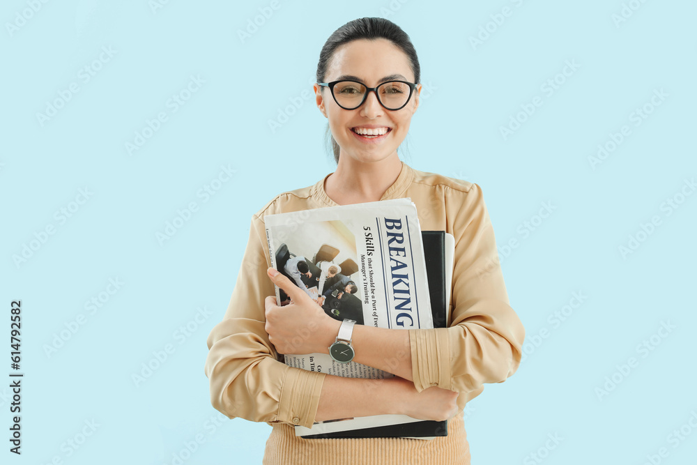 Young businesswoman with wristwatch, newspapers and laptop on blue background