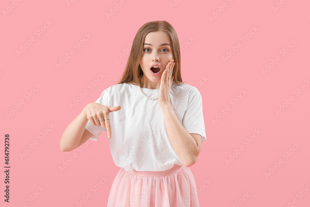 Shocked young woman pointing at something on pink background