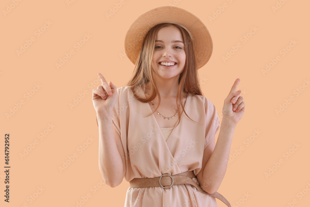 Young woman in hat pointing at something on beige background