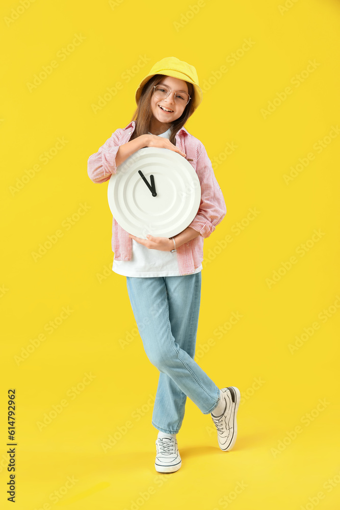 Little girl with wall clock on yellow background