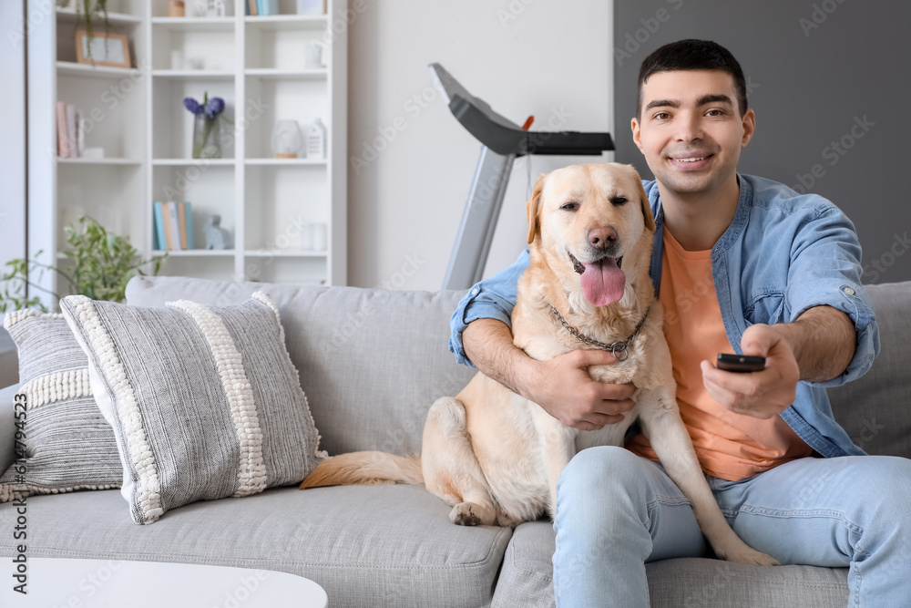 Young man with cute Labrador dog watching TV on sofa at home