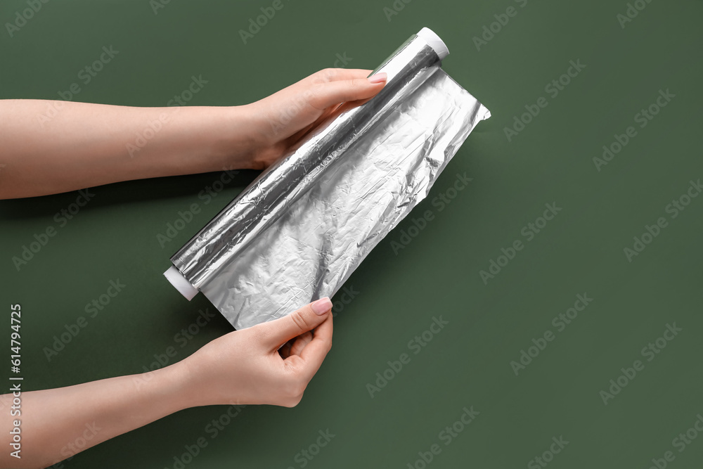 Female hands with roll of aluminium foil on green background