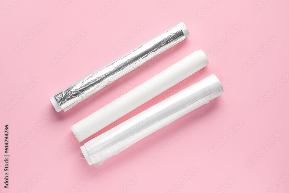 Rolls of aluminium foil, baking paper and food film on pink background