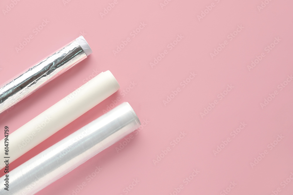 Rolls of aluminium foil, baking paper and food film on pink background