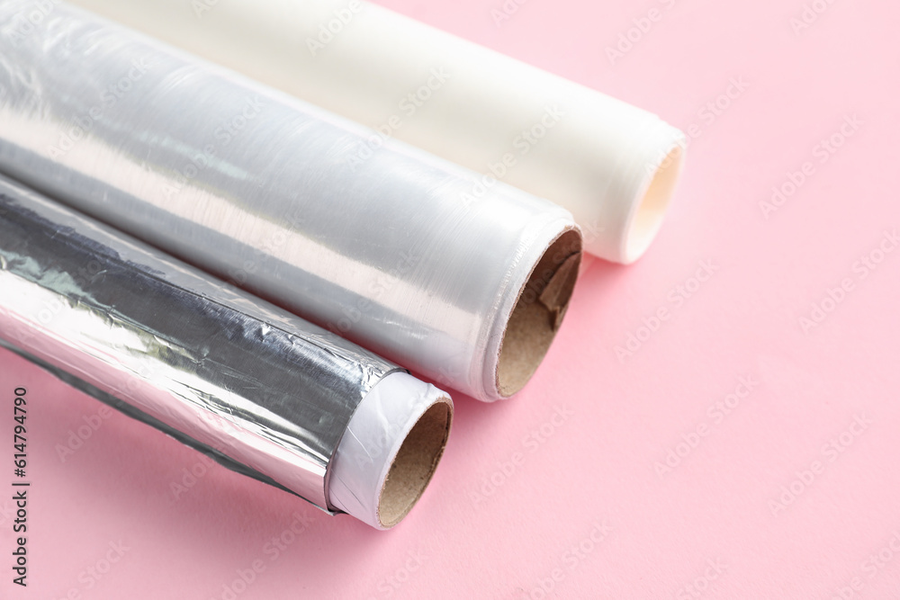 Rolls of aluminium foil, baking paper and food film on pink background, closeup