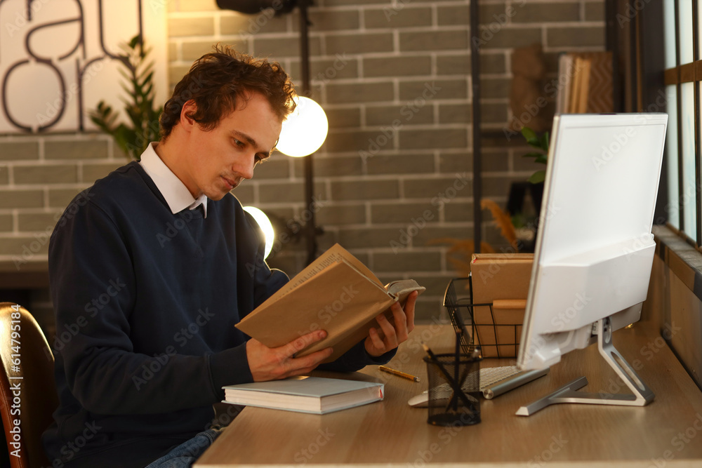 Young man reading book at table late in evening