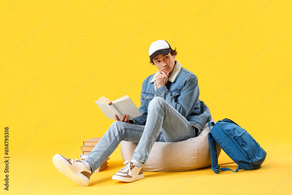 Male student reading book on yellow background