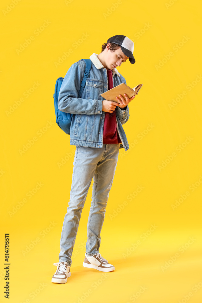 Male student reading book on yellow background