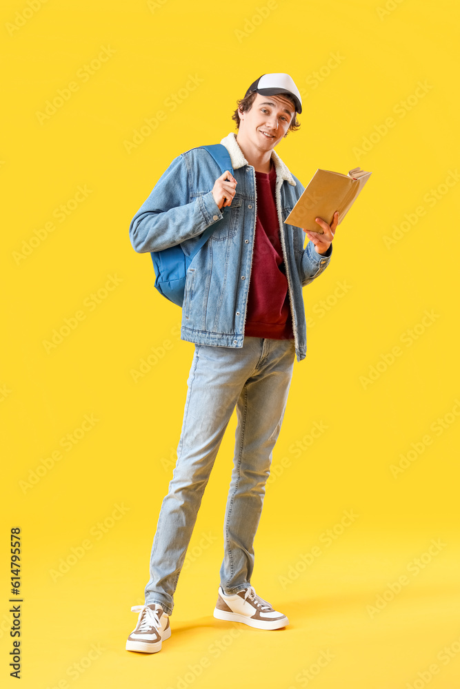 Male student reading book on yellow background