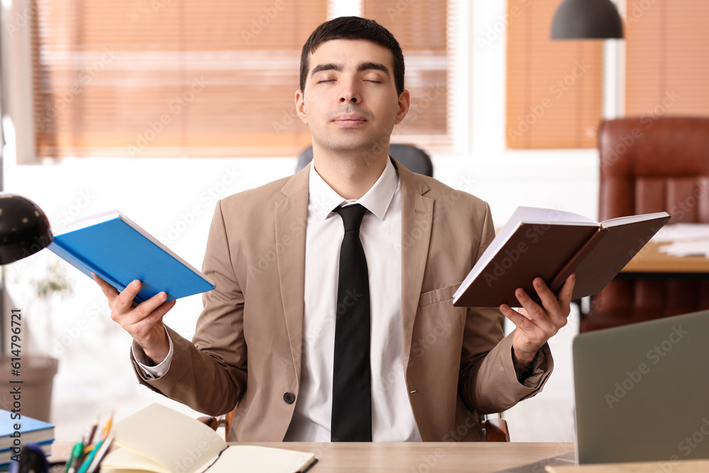 Young businessman with books meditating in office. Balance concept