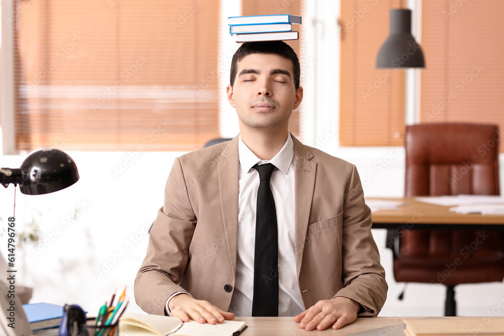 Young businessman with books meditating in office. Balance concept