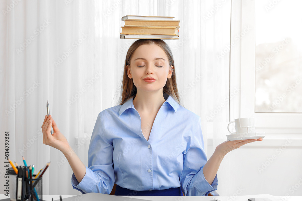 Young businesswoman with books, pen and cup of coffee meditating in office. Balance concept