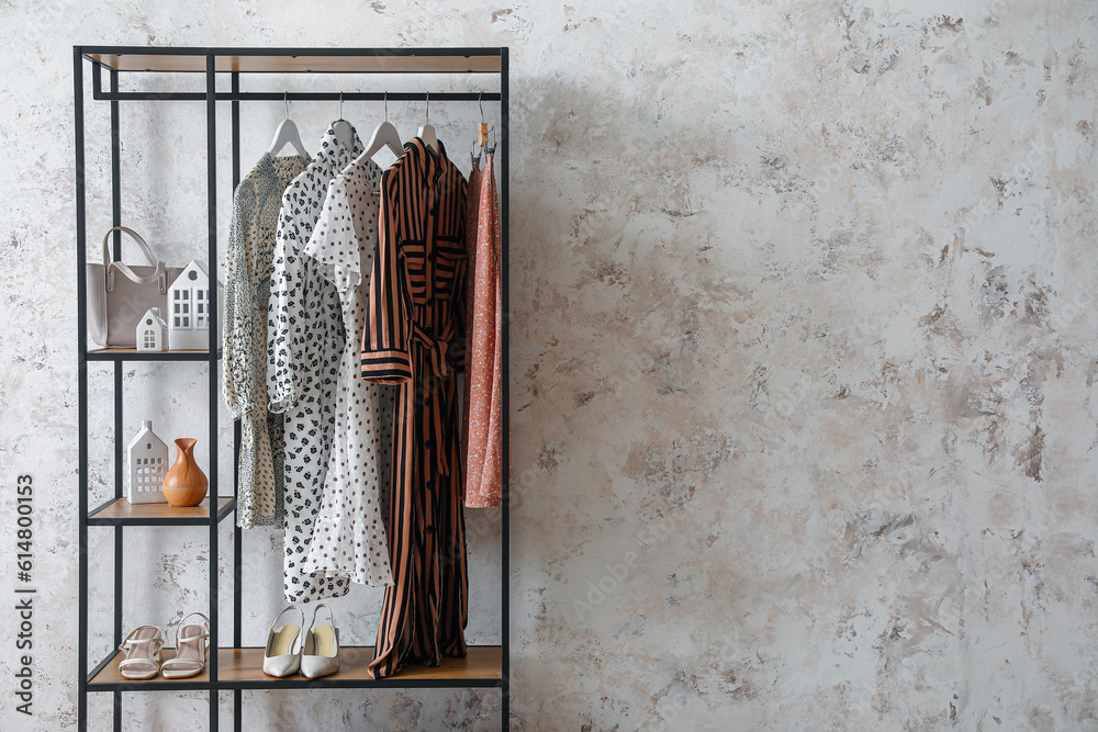 Shelving unit with clothes, shoes and bag near light wall