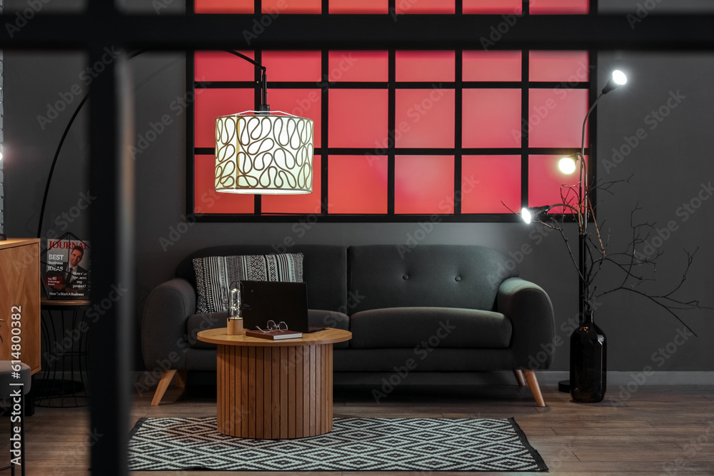 Interior of stylish living room with black sofa and modern laptop on coffee table, view through fold