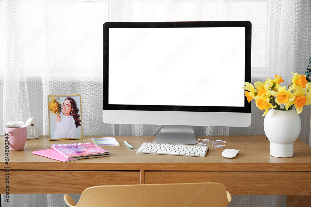 Comfortable workplace with modern PC and narcissus flowers near window