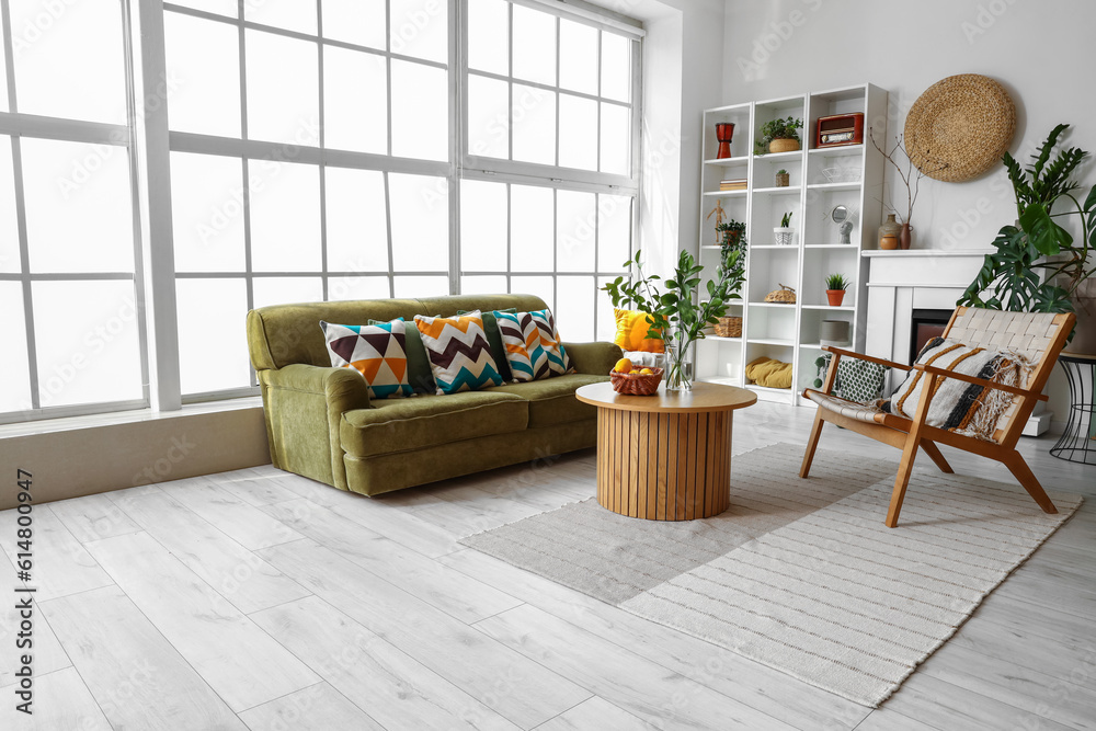 Interior of bright living room with cozy sofa, armchair and coffee table near big window