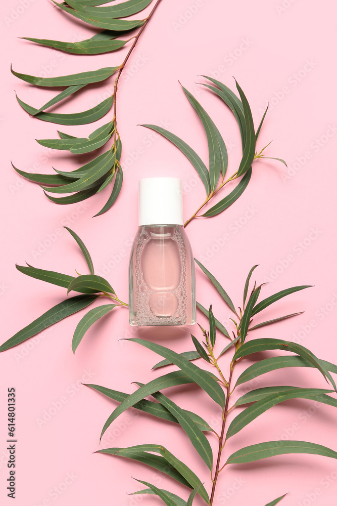 Bottle of micellar water with plant branches on pink background