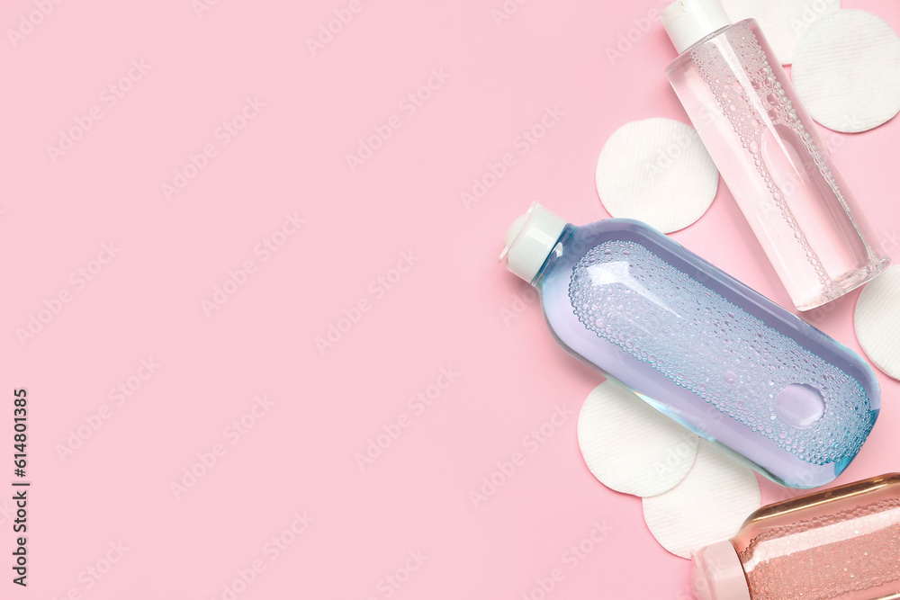 Bottles of micellar water with cotton pads on pink background