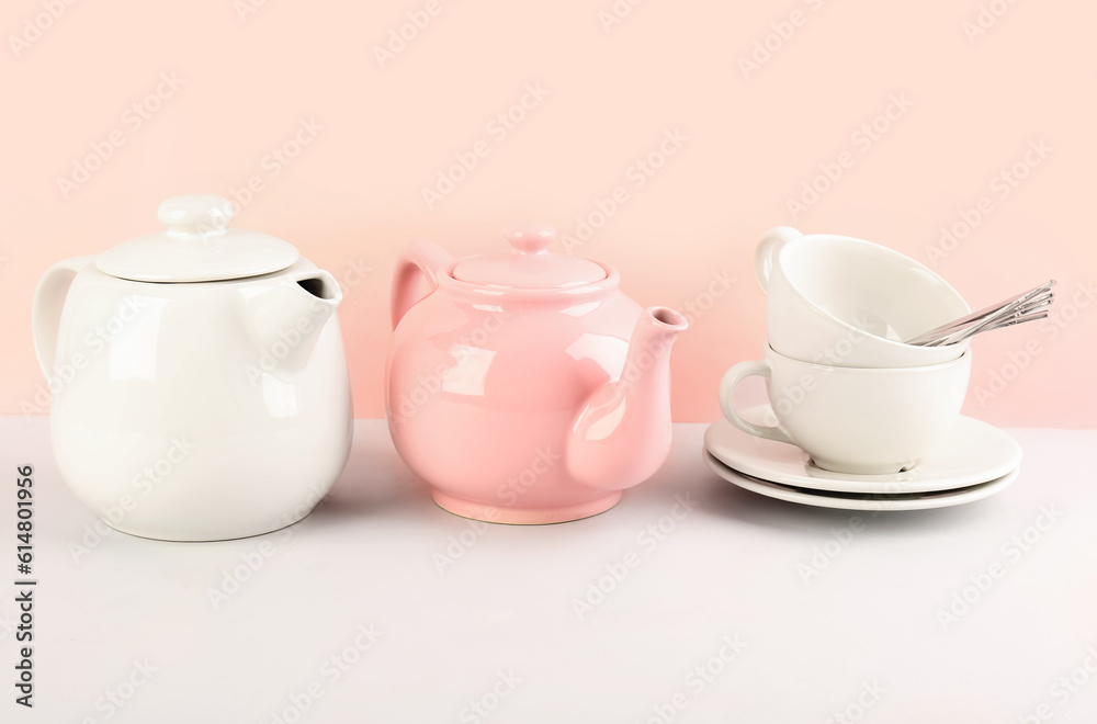 Teapots and cups with spoons on pink background