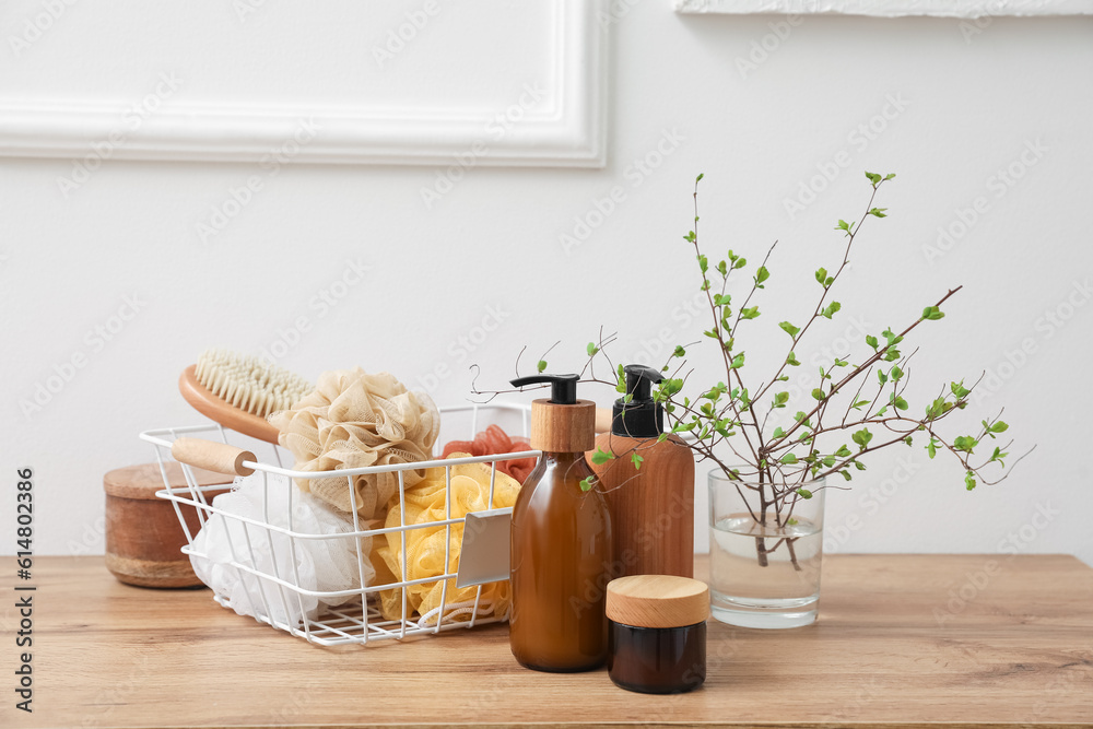 Bath accessories and vase with tree branches on table near light wall