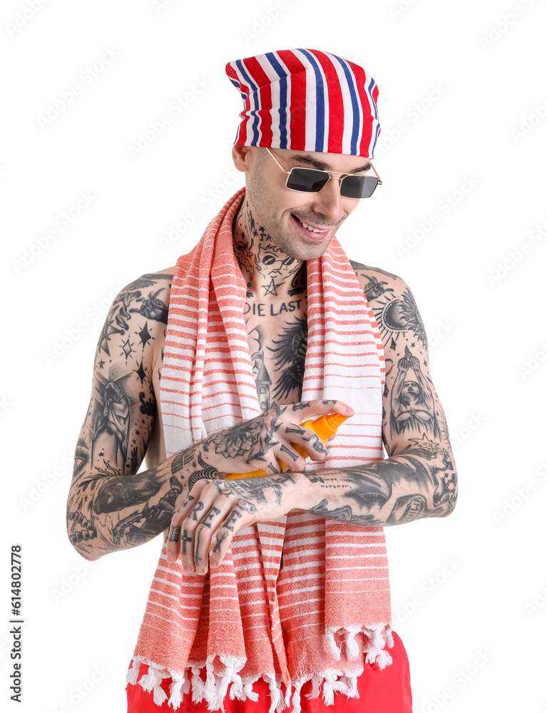 Tattooed man applying sunscreen cream on white background