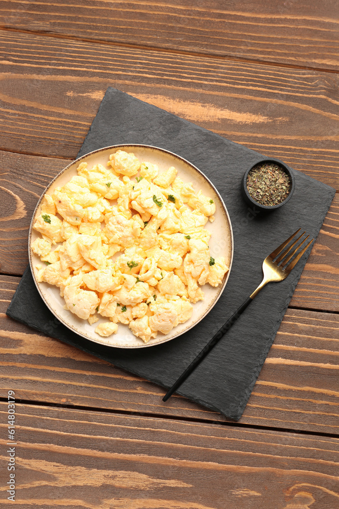 Plate of delicious scrambled eggs with spices on brown wooden background