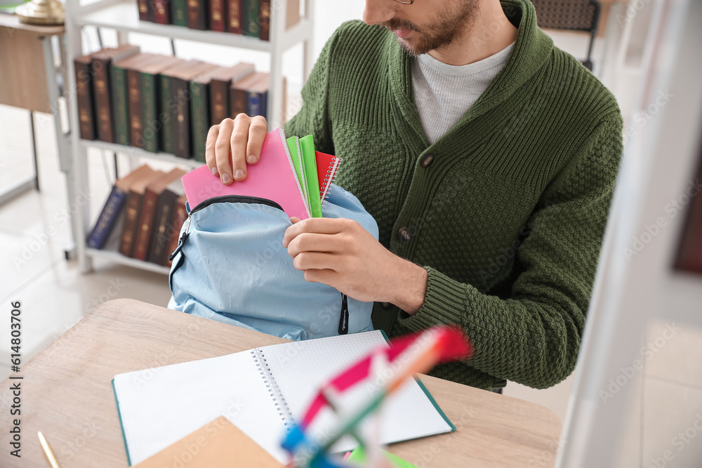 Male student taking copybooks from backpack in library, closeup