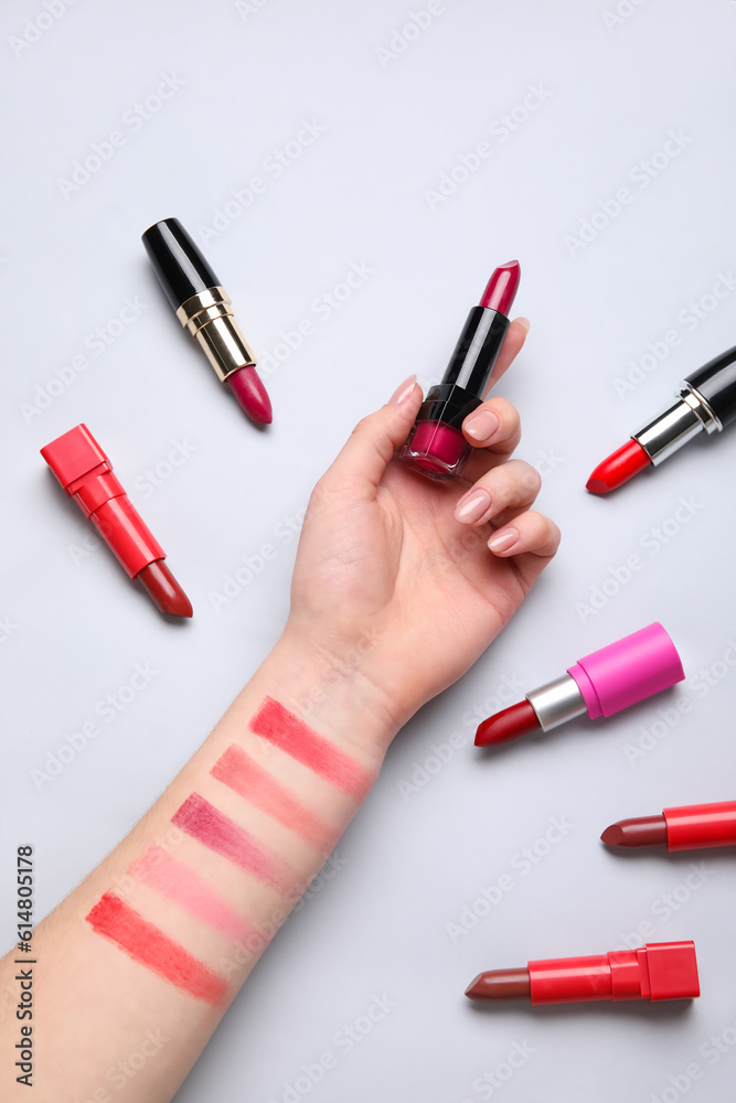 Woman with lipsticks and samples on light background