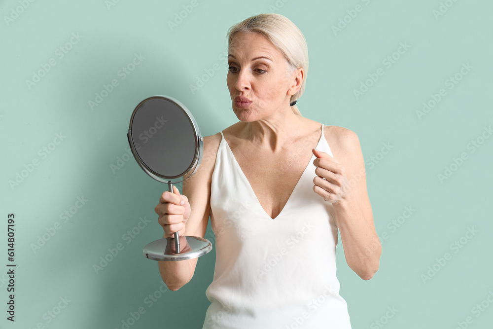 Mature woman with mirror doing face building exercise on green background