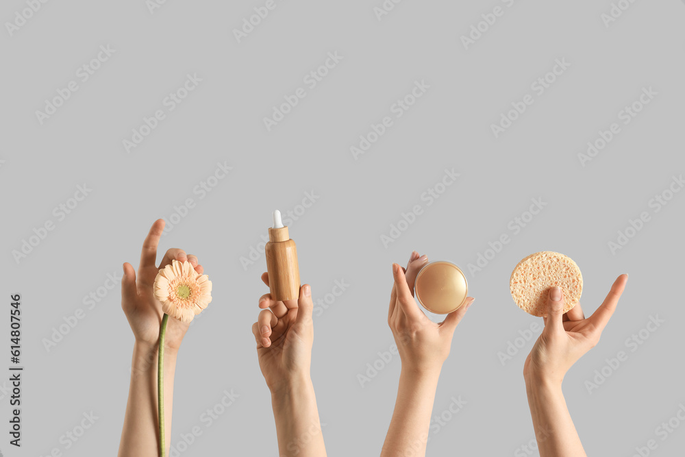 Hands holding different cosmetic products and flower on light background