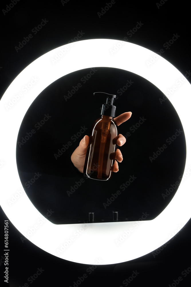 Hand holding bottle of cosmetic product on dark background