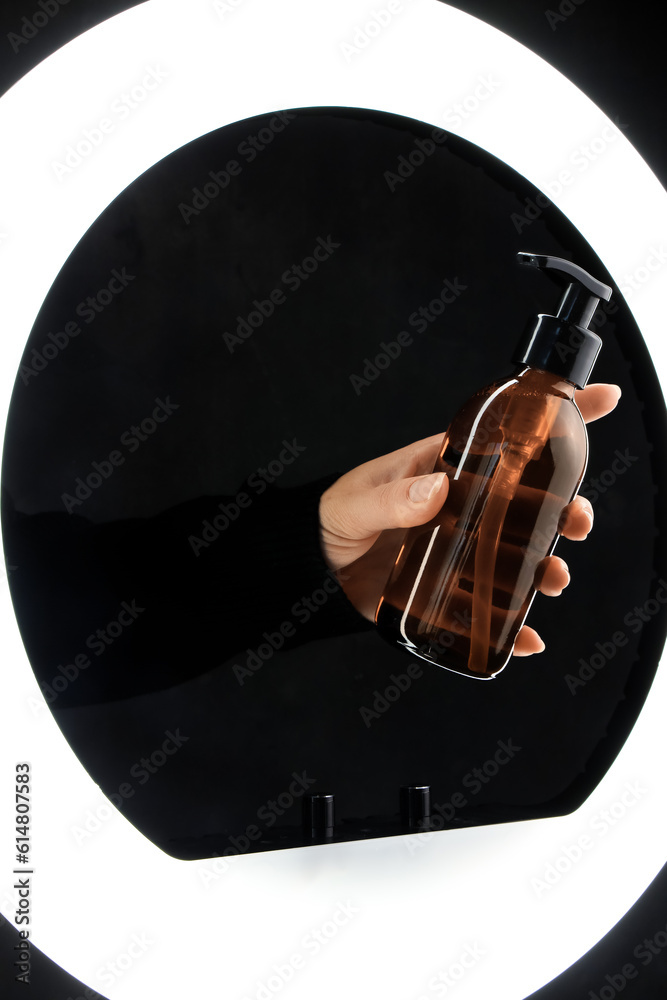 Hand holding bottle of cosmetic product on dark background