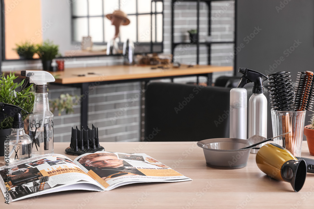 Different hairdressing tools and magazine on table in beauty salon