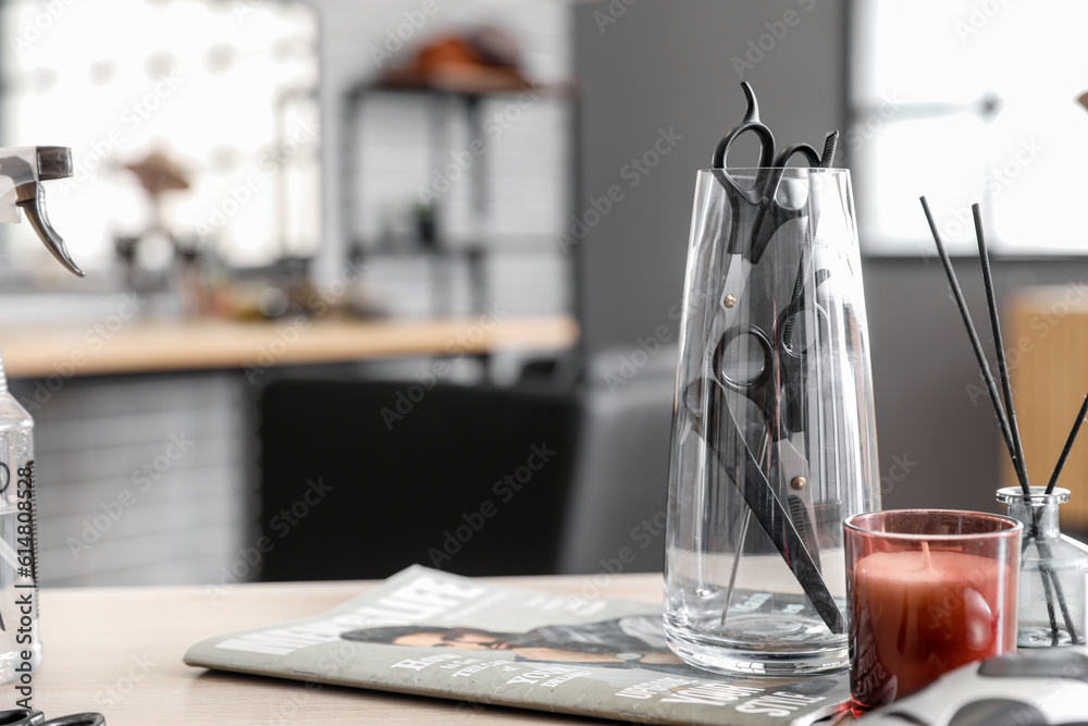 Glass with different hairdressing tools and candle on table in beauty salon