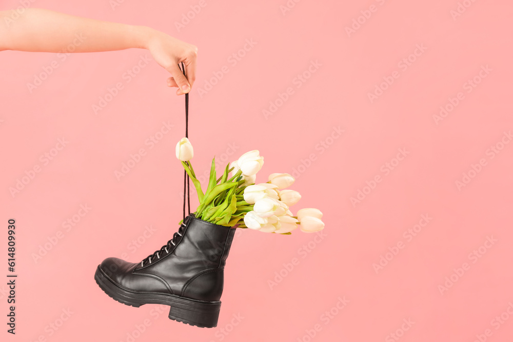 Female hand with tulip flowers in shoes on pink background