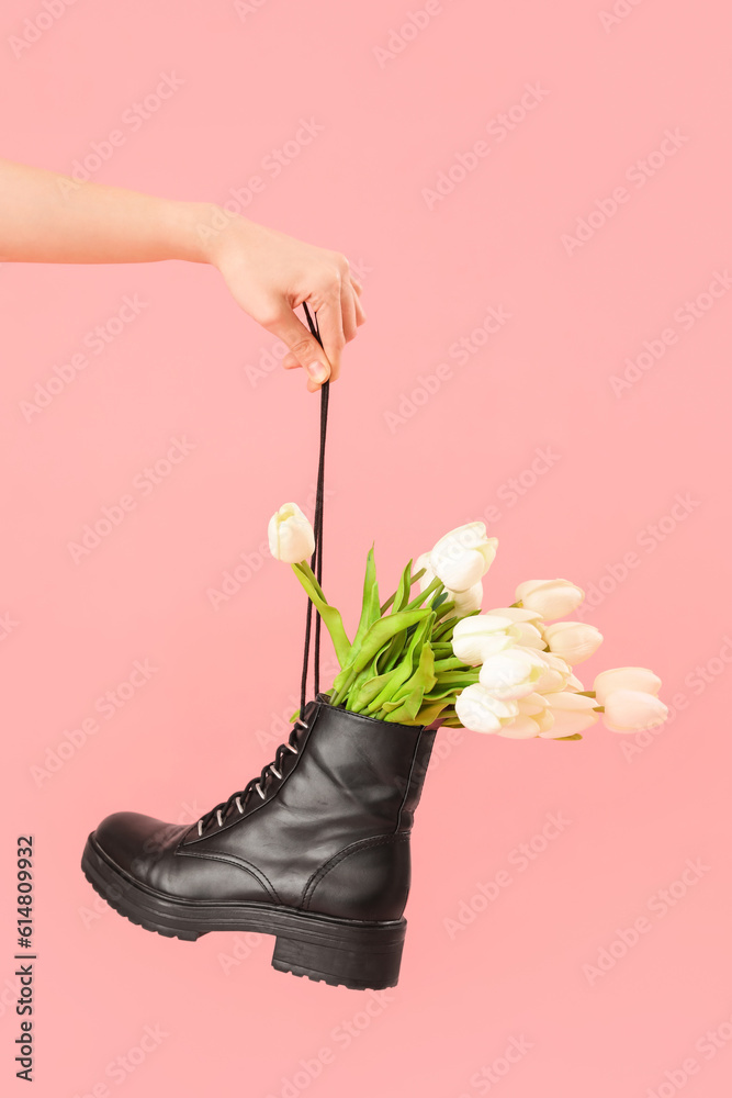 Female hand with tulip flowers in shoes on pink background