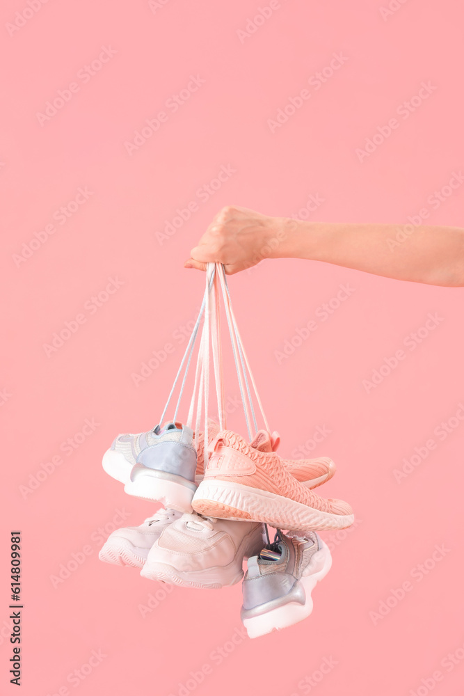 Female hand with many sneakers on pink background