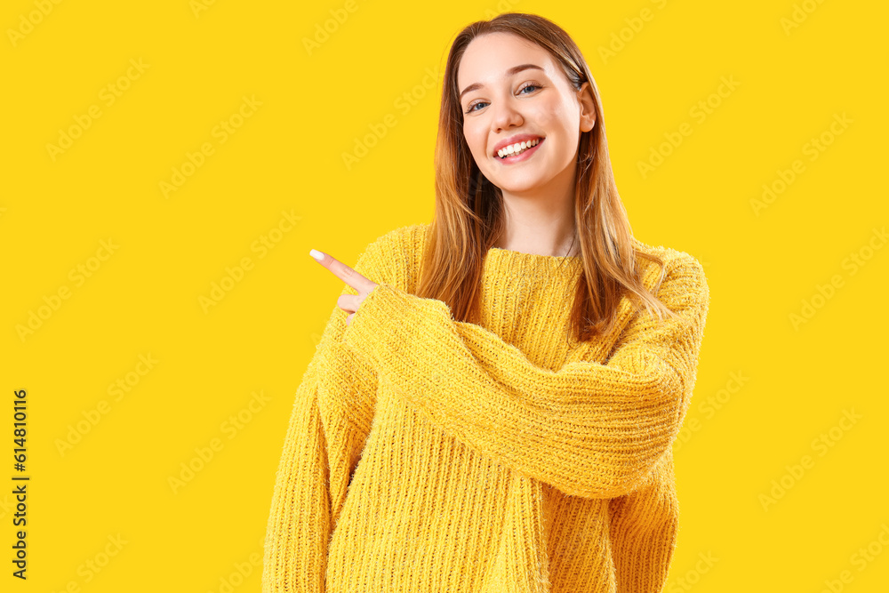 Beautiful young woman pointing at something on yellow background